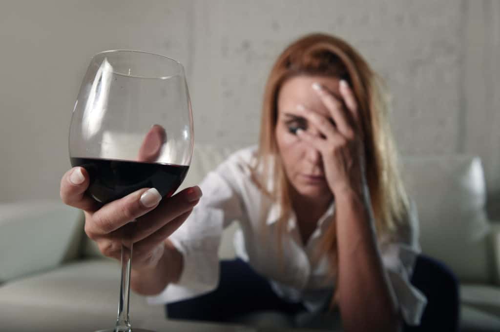 woman with headache holding glass of red wine