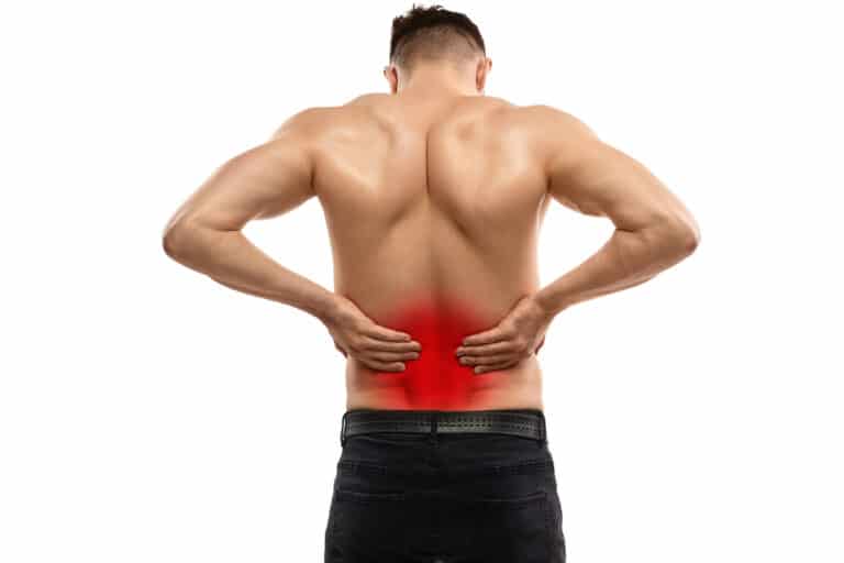 Back view of young muscular man rubbing highlighted area on lower back with both hands while suffering from spine pain against white background