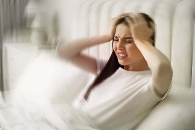 Young woman suffering from migraine in bed at home vertigo causing dizziness