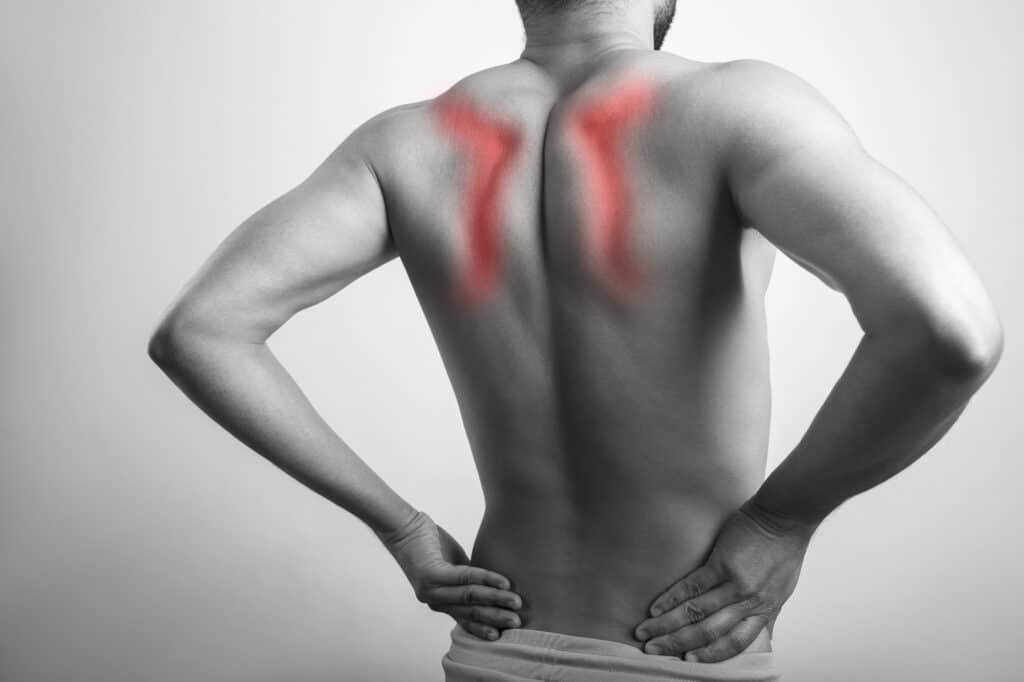 Monochrome male shirtless body pain, shoulder blade injury. Shirtless young man inflamed on scapula injury area highlighted in red glow.